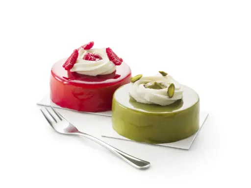 Deux petits gâteaux brillants, l'un rouge vif, l'autre vert avec un glaçage pistache, ornés de crème et de fruits.
