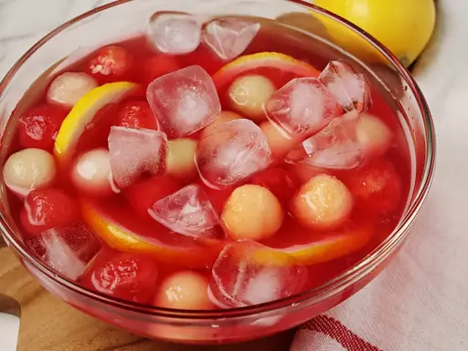 Erfrischende melonenbowle ohne alkohol mit Eiswürfeln, Melonenbällchen und Zitronenscheiben in einer Glasschüssel.