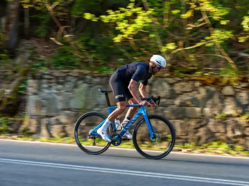 Kolarz w kasku ściga się na niebieskim rowerze Canyon Endurace CF 7 po malowniczej drodze wśród zieleni.