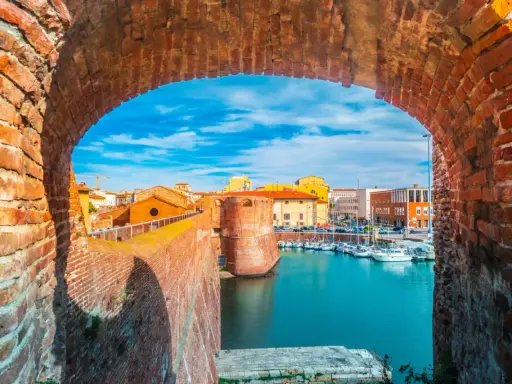 Widok na port w Livorno przez ceglany łuk. Widać łodzie, budynki i fortyfikacje. Idealne miejsce, by zobaczyć Livorno.