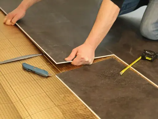 Pose de dalles de sol sur une sous-couche isolante. Un cutter et un mètre sont à portée de main pour comment isoler un sol efficacement.
