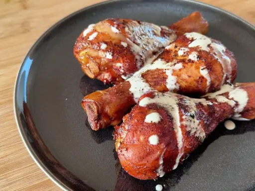 Tre succulenti fusi di pollo arrostiti, conditi con spezie e nappati con una cremosa salsa bianca, serviti su un piatto scuro.