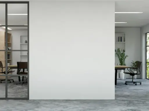 Un moderno tabique de cristal separa una sala de reuniones con estanterías de madera de una oficina con vistas a un jardín frondoso.