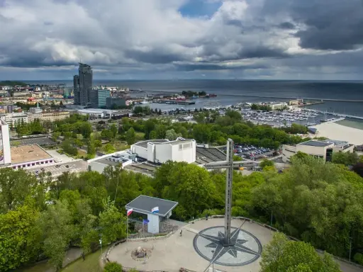 Gdynia co zobaczyć: pomnik z różą wiatrów i krzyżem na wzgórzu, w tle port, plaża i drapacze chmur.