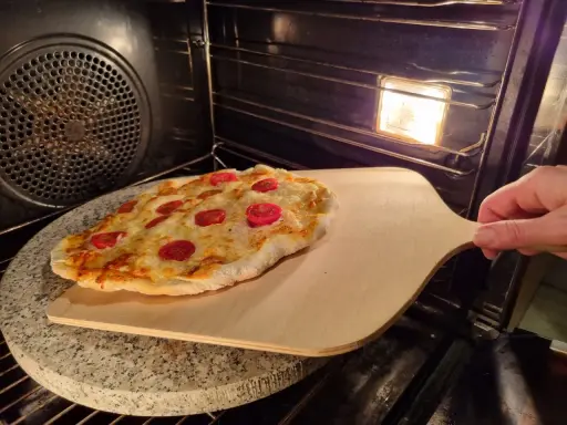 Pizza na kamieniu w piekarniku, gotowa do wyjęcia. Idealny sposób, jak piec pizzę na kamieniu dla chrupiącego spodu.