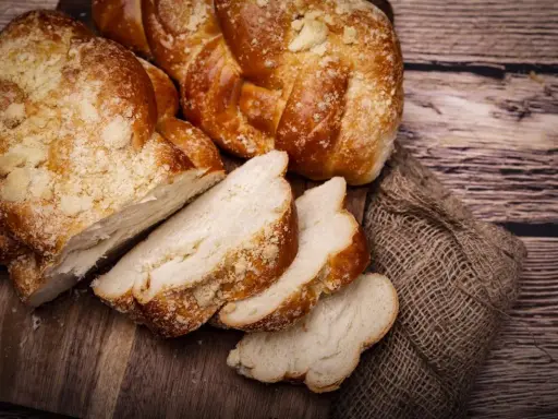 Puszyste ciasto drożdżowe, pokrojone w kromki, na drewnianej desce. Dowiedz się, jak przechowywać ciasto drożdżowe, by było świeże.