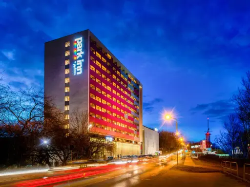 Wieczorem rozświetlony hotel Park Inn w Katowicach z kolorowym logo. Na ulicy widać światła samochodów.