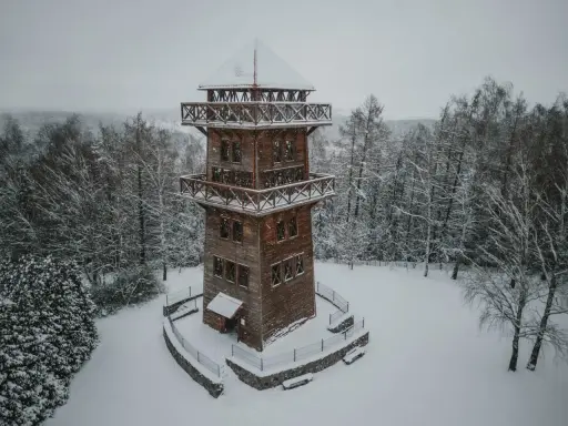 Drewniana wieża widokowa na Mazurach w zimowej scenerii. Otoczona ośnieżonym lasem, zaprasza do podziwiania krajobrazu.