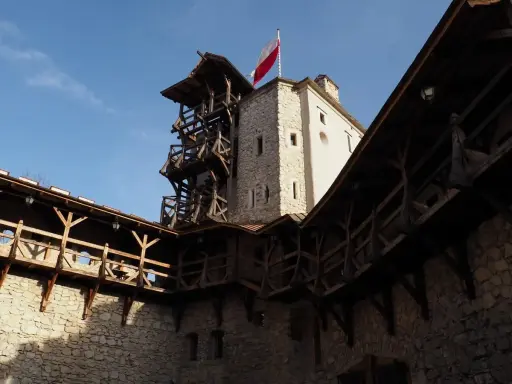 Zamek w Korzkwi z drewnianymi gankami i wieżą, na której powiewa polska flaga.