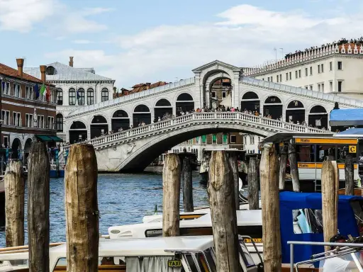 Le célèbre pont du Rialto à Venise, animé par des touristes, surplombe le Grand Canal où naviguent des gondoles et des taxis nautiques.