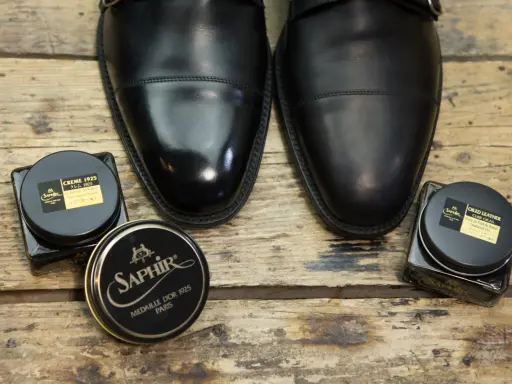 Czarne, eleganckie buty i dwa słoiczki Saphir: krem do skóry i olejek. Idealne, by dowiedzieć się, czym natłuścić skórzane buty.