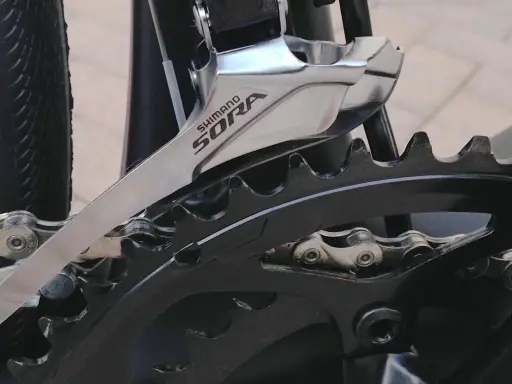 Montaż przedniej przerzutki Shimano Sora na rowerze. Widoczny fragment mechanizmu korbowego i łańcucha.