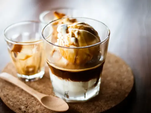 Ein italienischer Eiskaffee, Affogato, mit Vanilleeis und heißem Espresso. Ein Holzlöffel liegt daneben.