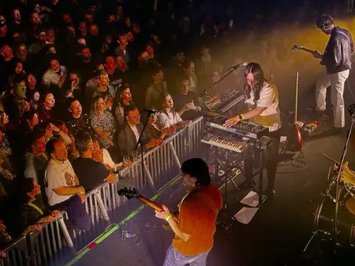 Publik njuter av Altin Gün i Stockholm. En gitarrist spelar, en keyboardist bakom Roland-syntar, och en entusiastisk publik bakom stängsel.