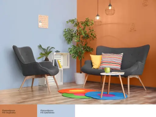 Nowoczesny salon z szarymi fotelami i kanapą, akcentem jest ściana w kolorze oranżowym.