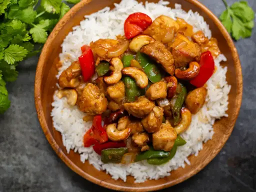 Un délicieux poulet noix de cajou servi sur un lit de riz blanc. Des poivrons rouges et verts ajoutent de la couleur à ce plat savoureux.