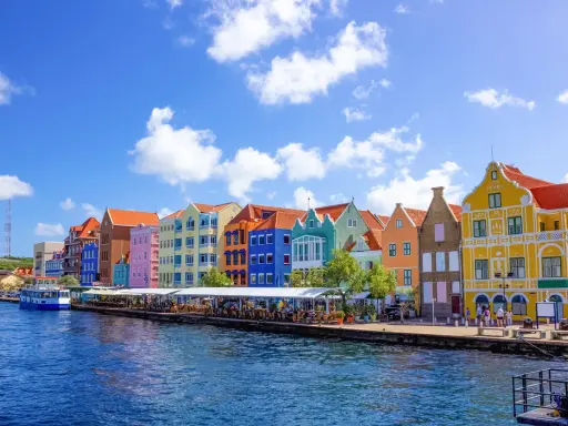 Färgstarka hus längs en kaj, en båt i vattnet. Här kan man se var ligger Curacao, en karibisk pärla.
