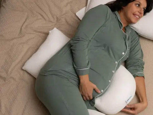 Donna incinta, con pigiama verde, si rilassa a letto con un cuscino di supporto, alleviando la stanchezza in gravidanza.