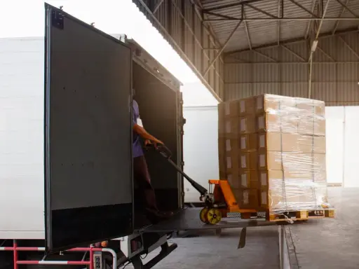 Un operario usa una carretilla para el transporte de materiales, cargando cajas en un camión.