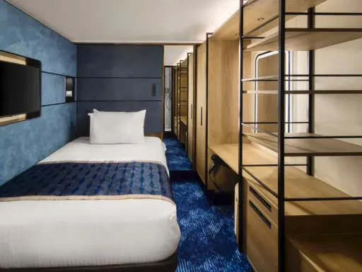 Interno cabina singola nave da crociera: letto, TV a parete, armadio aperto con mensole e scrivania. Le dimensioni delle cabine sono ottimizzate per il comfort.