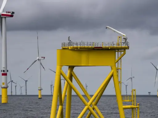 Große gelbe Plattform mit Kran inmitten vieler Windkraftanlagen im Meer. Die Zukunft der Windkraft onshore und offshore.