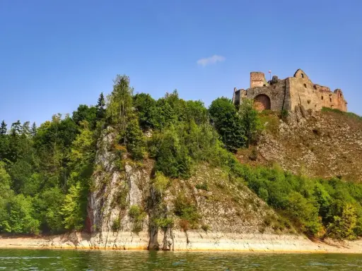 Zamek Czorsztyn góruje nad jeziorem, otoczony zielenią. Ruiny zamku na skale, widok z wody.