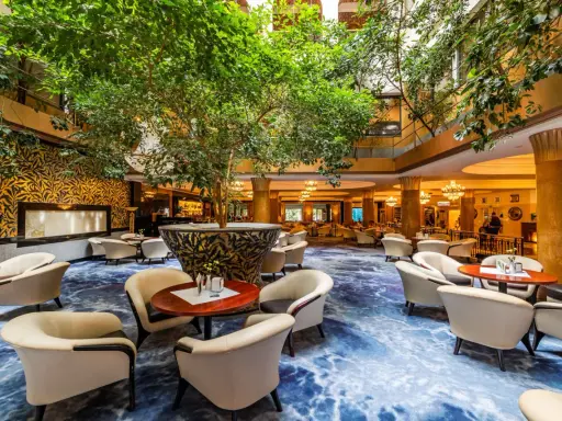 Luksusowy hol hotelowy z bujną roślinnością, wygodnymi fotelami i ozdobnym dywanem. Idealne miejsce na relaks w sieci luksusowych hoteli.