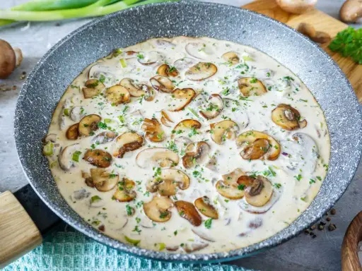 Cremige Rahmsauce mit frischen Champignons, verfeinert mit Petersilie, in einer Pfanne.