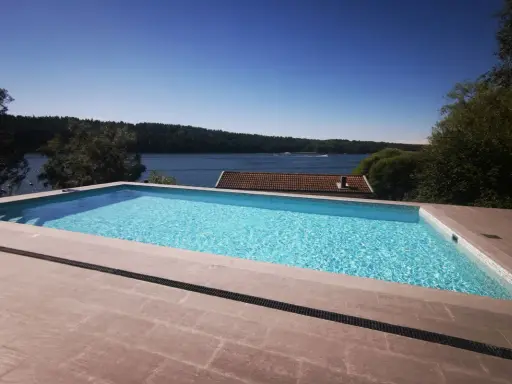 En lyxig pool med klarblått vatten och en fantastisk utsikt över en sjö. En dröm för många, men vad är bygga pool kostnad?