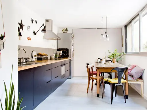 Cuisine salle à manger en longueur avec meubles sombres, plan de travail en bois, table en bois et banquette.