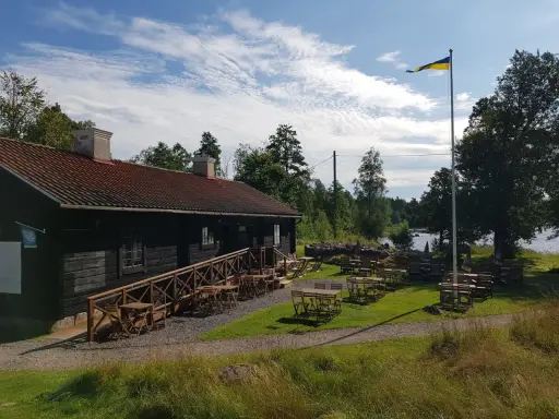 Mysigt tiveden boende med uteservering vid vattnet. En svensk flagga vajar i vinden.