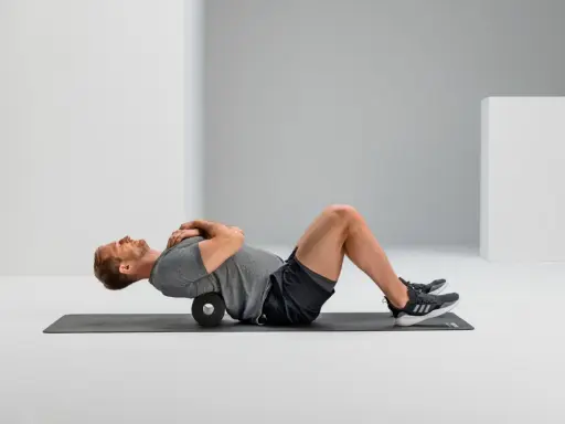 Mann macht Foam Rolling auf einer Matte, um seinen Rücken zu entspannen.