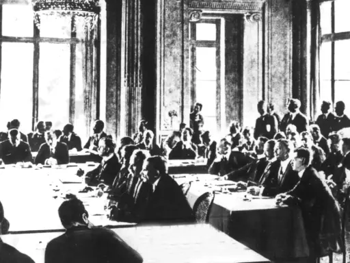 Männer in Anzügen sitzen an langen Tischen in einem prunkvollen Saal. Dies ist die Unterzeichnung des Versailler Vertrags, der den Ersten Weltkrieg beendete.