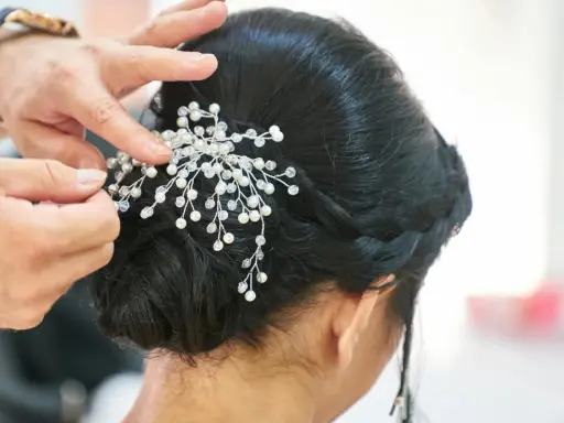Manos expertas ajustan un tocado de perlas y cristales a un juvenil recogido de boda, creando un look elegante y romántico.