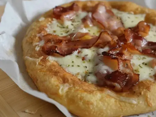 Pyszna pizza z mozzarellą i chrupiącym boczkiem, posypana ziołami. Idealna na szybki lunch.