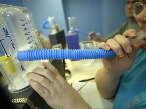 Person nutzt ein Spirometer für einen Lungenfunktionstest. Der Asthmaspray ist nicht sichtbar, aber das Gerät hilft bei der Diagnose.