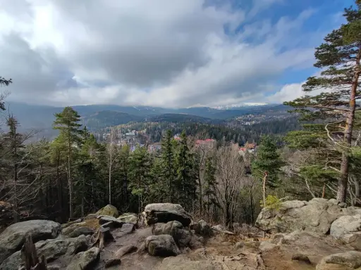 Widok na Karpacz zalesionymi wzgórzami i górami w tle, z kamienistym pierwszym planem.
