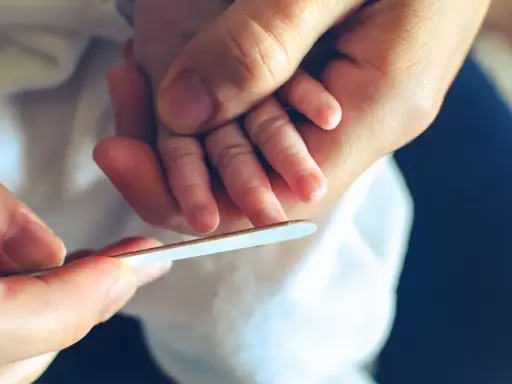 Mani adulte limano delicatamente le unghie di un neonato, un momento di cura che mostra quando si possono tagliare le unghie ai neonati.