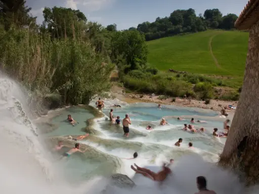Persone si rilassano nelle cascate naturali delle **Terme di Saturnia**, immerse nel verde della campagna toscana.