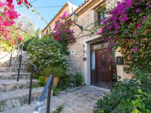 Escaleras de piedra adornadas con buganvillas y flores blancas, que llevan a la entrada de una casa de piedra. Un ejemplo de los pueblos bonitos de Alicante.