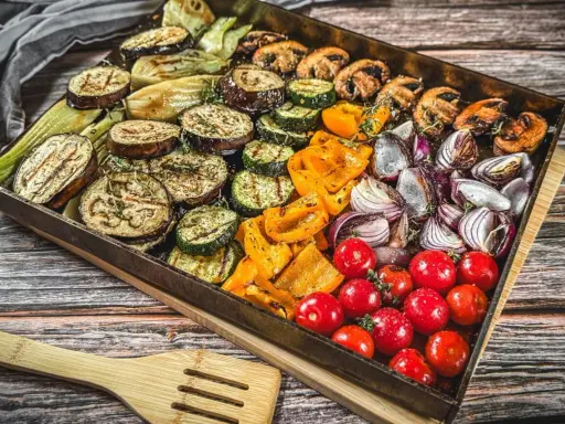 Buntes Gemüse wie Auberginen, Zucchini, Paprika, Zwiebeln und Tomaten auf einem Blech für ein köstliches vegetarisches Grillen.