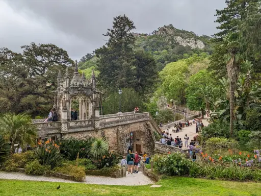 Ein märchenhafter Sintra Garten mit einer steinernen Brücke, üppiger Vegetation und Besuchern, die die Aussicht genießen.
