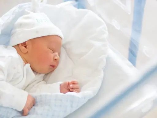 Śpiący noworodek w szpitalnym łóżeczku. Do wniosku o becikowe potrzebne są dokumenty potwierdzające urodzenie dziecka.