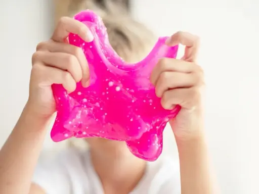 Dziecko bawi się różowym slime, który wygląda jak z przepisu na domowy slime.