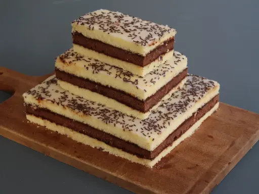 Trois parts de napolitain sans gluten empilées sur une planche en bois, garnies de vermicelles au chocolat.