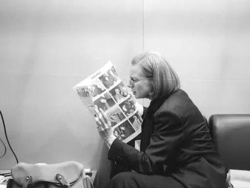 Fleur Jaeggy, con occhiali e giacca scura, legge un giornale con foto.