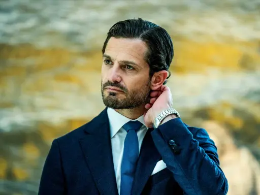 Prins Carl Philip i mörkblå kostym, vit skjorta och blå slips. Hans hand vilar bakom örat, en detalj som speglar hans intresse för carl philip design.