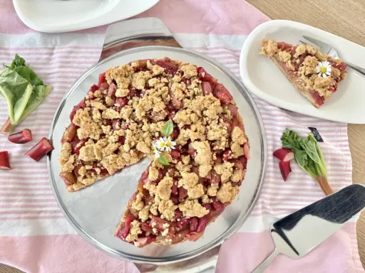 Ein köstlicher Rhabarber Streuselkuchen mit frischem Rhabarber und knusprigen Streuseln, garniert mit kleinen Gänseblümchen.
