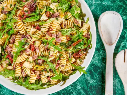 Pyszna sałatka z makaronem fusilli, rukolą, suszonymi pomidorami, oliwkami i kawałkami salami. Idealna na letnie dni.