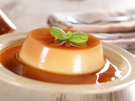 Un délicieux panna cotta caramel, nappé de sauce et garni d'une feuille de menthe. Un dessert onctueux et gourmand.